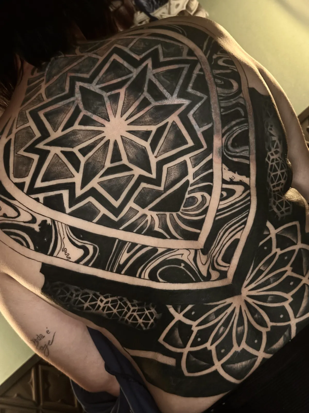 Tatuagem de mandala geométrica nas costas, detalhe da simetria radial
